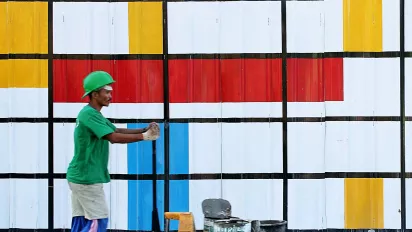 Man pushing a cart with paint buckets in front of a colourful wall.