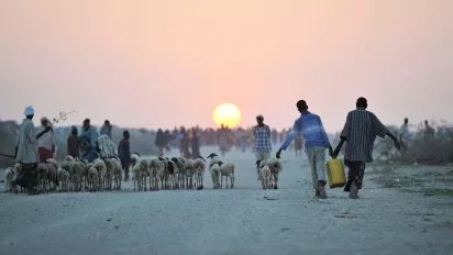 Two young boys carrying water walk down a road next to a camp for internally displaced persons in Somalia.