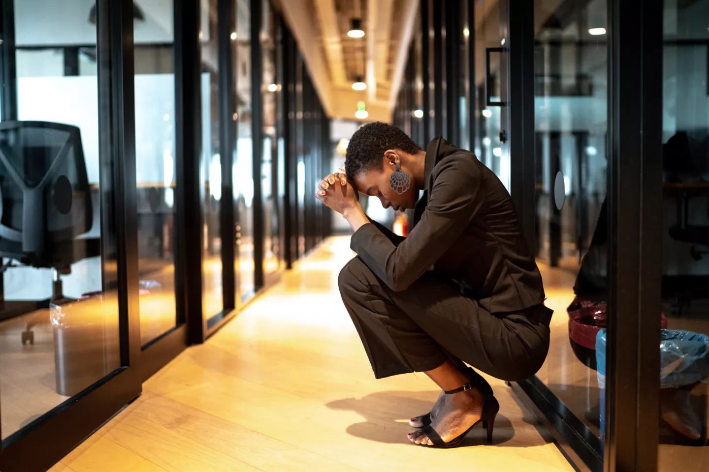 Jeune femme d'affaires accroupie, la tête dans les mains, dans le couloir d'un bureau