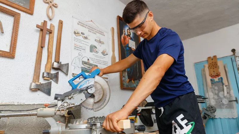 Young male wearing safety googles while using electric saw